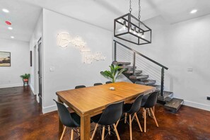 Een moderne eethoek met een houten tafel, zwarte stoelen, een geometrische hanglamp en een trap.