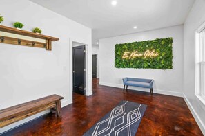 Een modern interieur met een houten bank, een geometrisch vloerkleed en een groene muur met een neonbord.