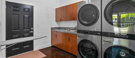 Una lavanderia con due lavasciuga affiancate, armadietti in legno, un piano di lavoro e una porta nera.