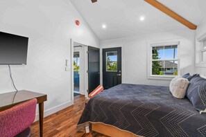 A bedroom with a bed, a desk, a chair, a window, and a door.
