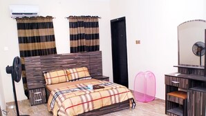 Una camera da letto con un letto, una ventola sul comodino, una cassettiera, uno specchio e tende.