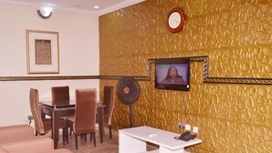 Una stanza con un tavolo da pranzo, sedie, un divano, una TV e una sveglia appesa al muro.