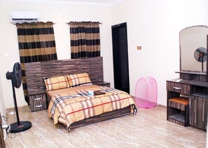A bedroom with a bed, a bedside fan, a dresser, a mirror, and curtains. - Immaculate 2-Bed Apartment in Idimu (Idimu)