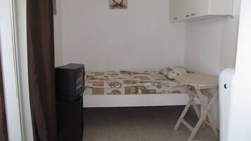 Habitación pequeña con una cama individual, televisor, mesa y armario.