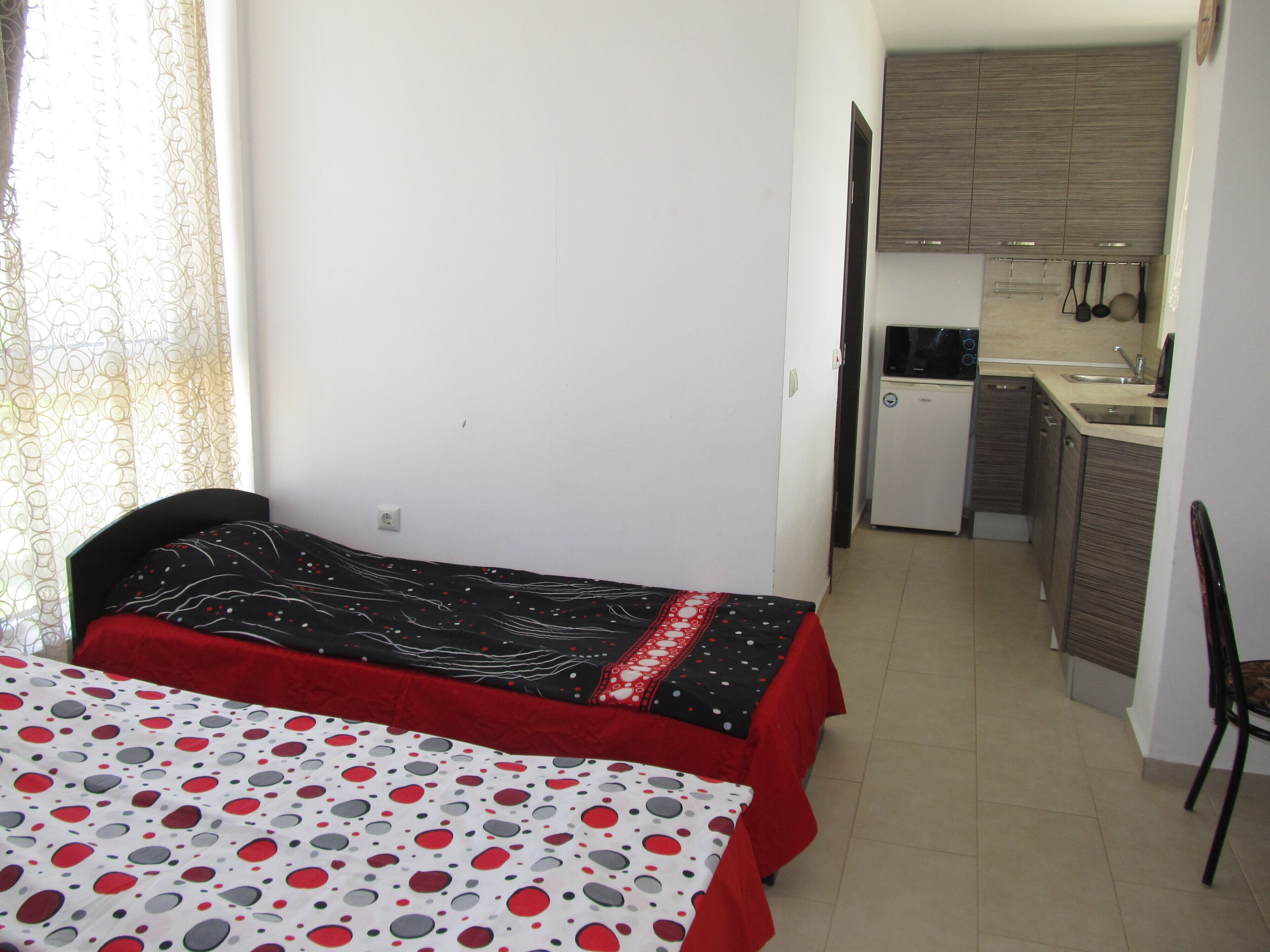 Una habitación pequeña y funcional con cama, kitchenette y una silla.