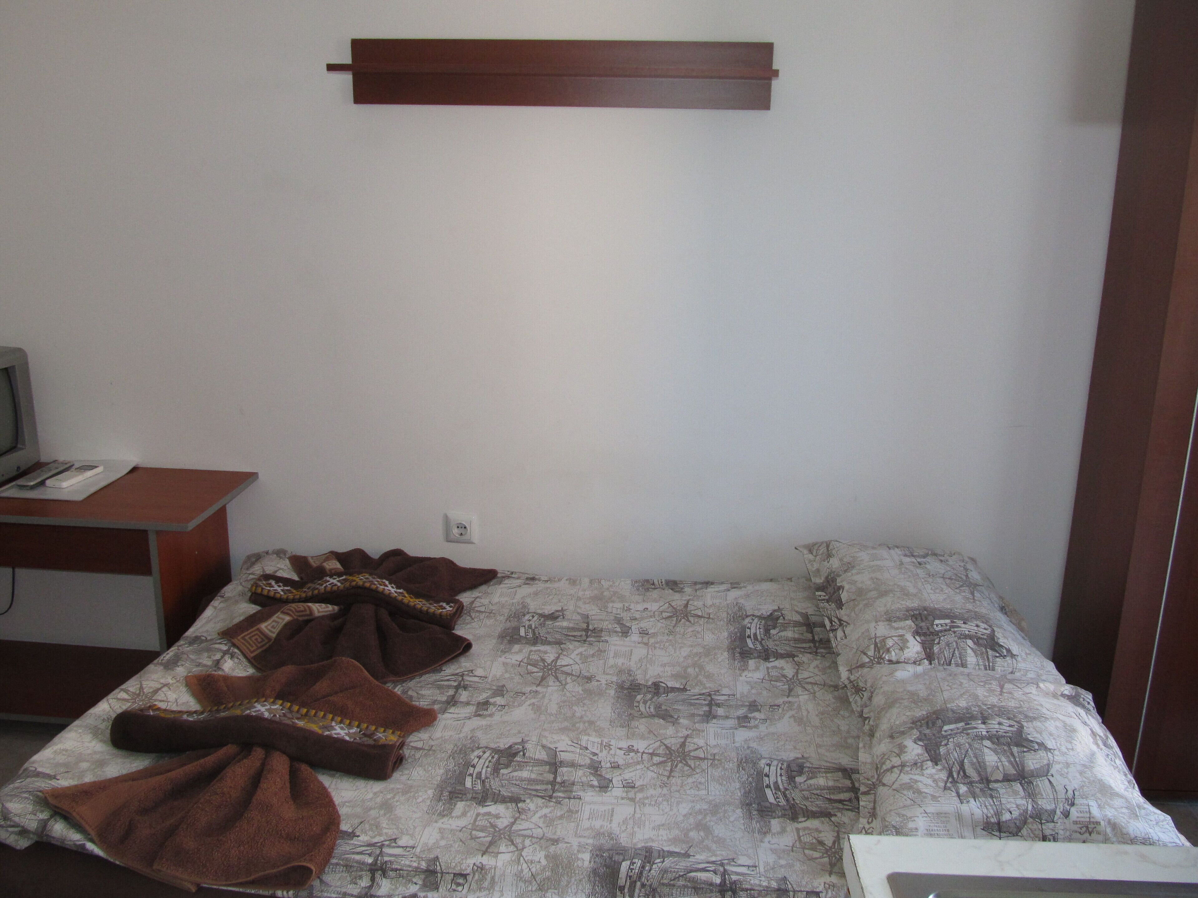A room with a bed, a desk with a computer, and a wall-mounted shelf.