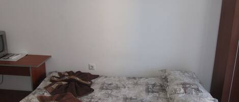 A room with a bed, a desk with a computer, and a wall-mounted shelf.
