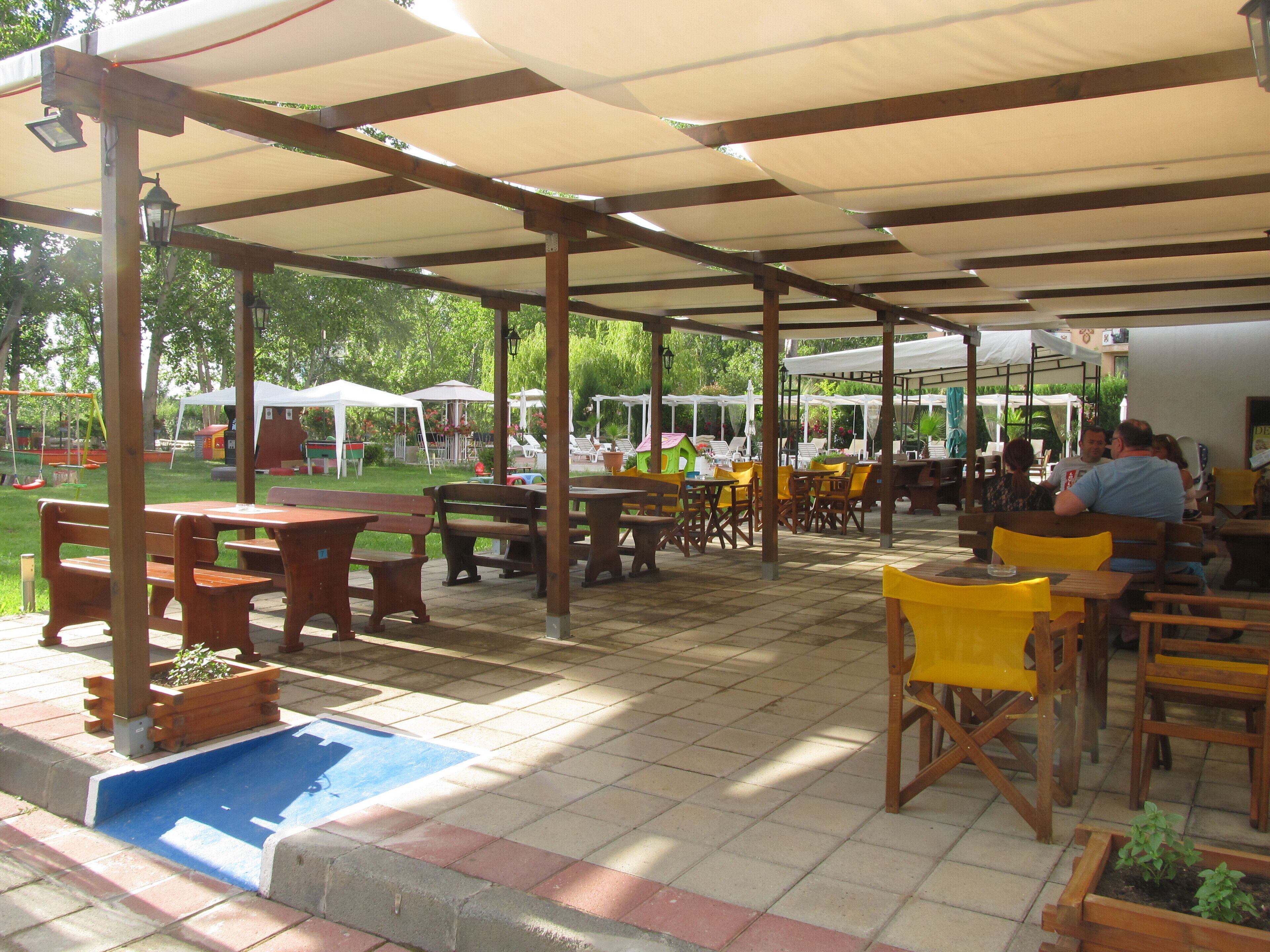 An outdoor patio area with wooden tables and benches, covered by a canopy.