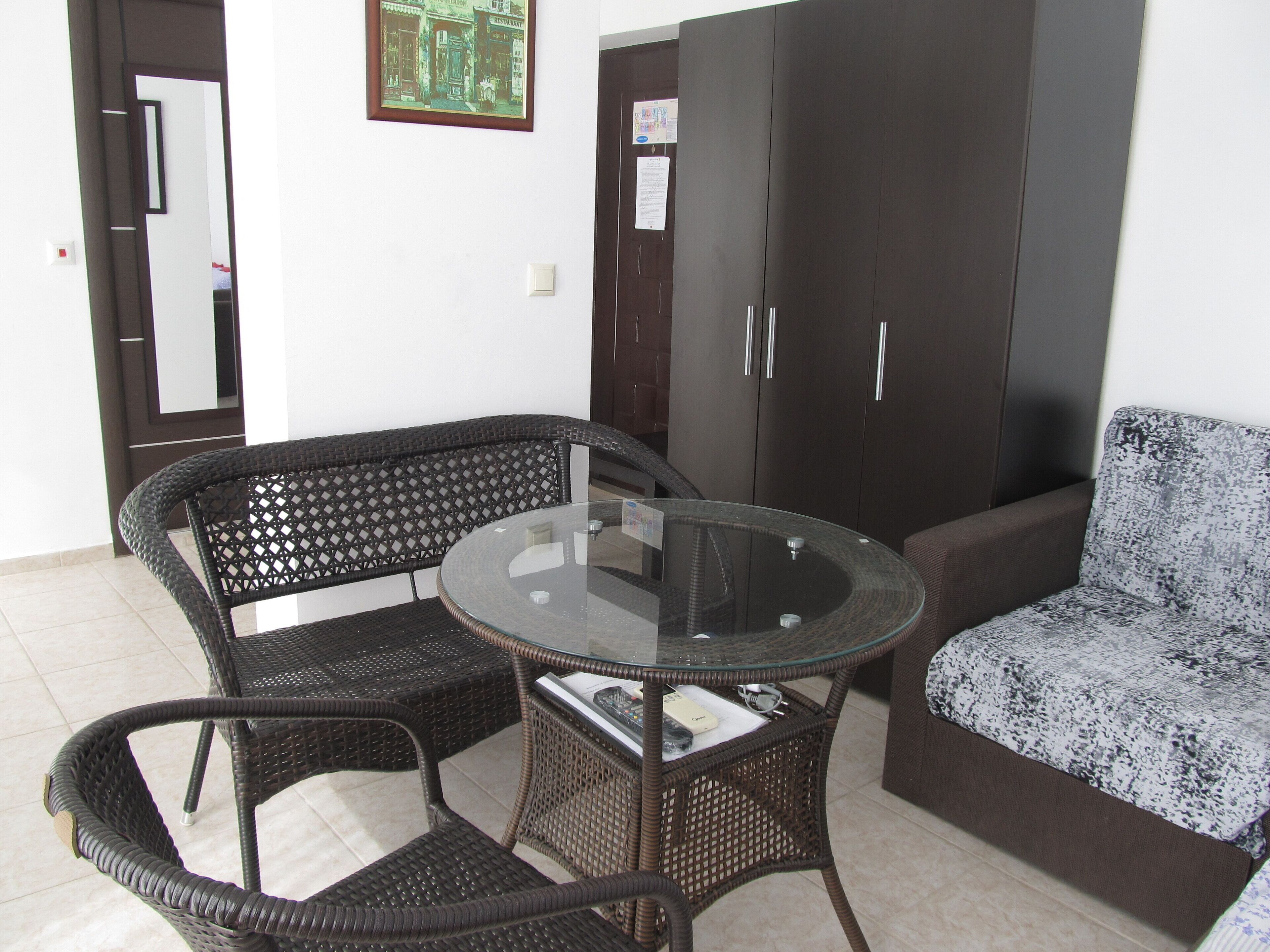 A room with a round glass table, two wicker chairs, a sofa, and a wardrobe.