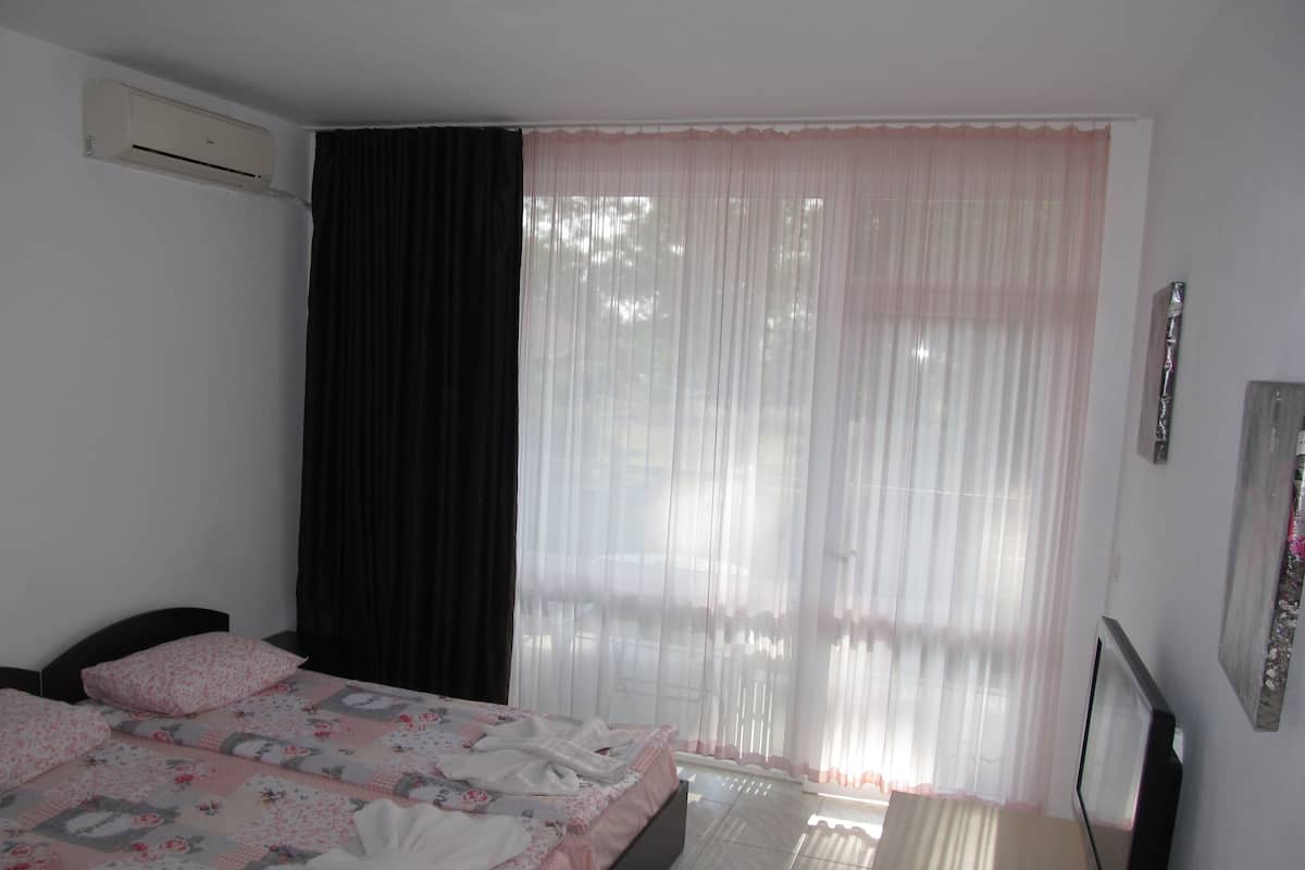 A bedroom with a bed, a TV, and a window with sheer curtains.