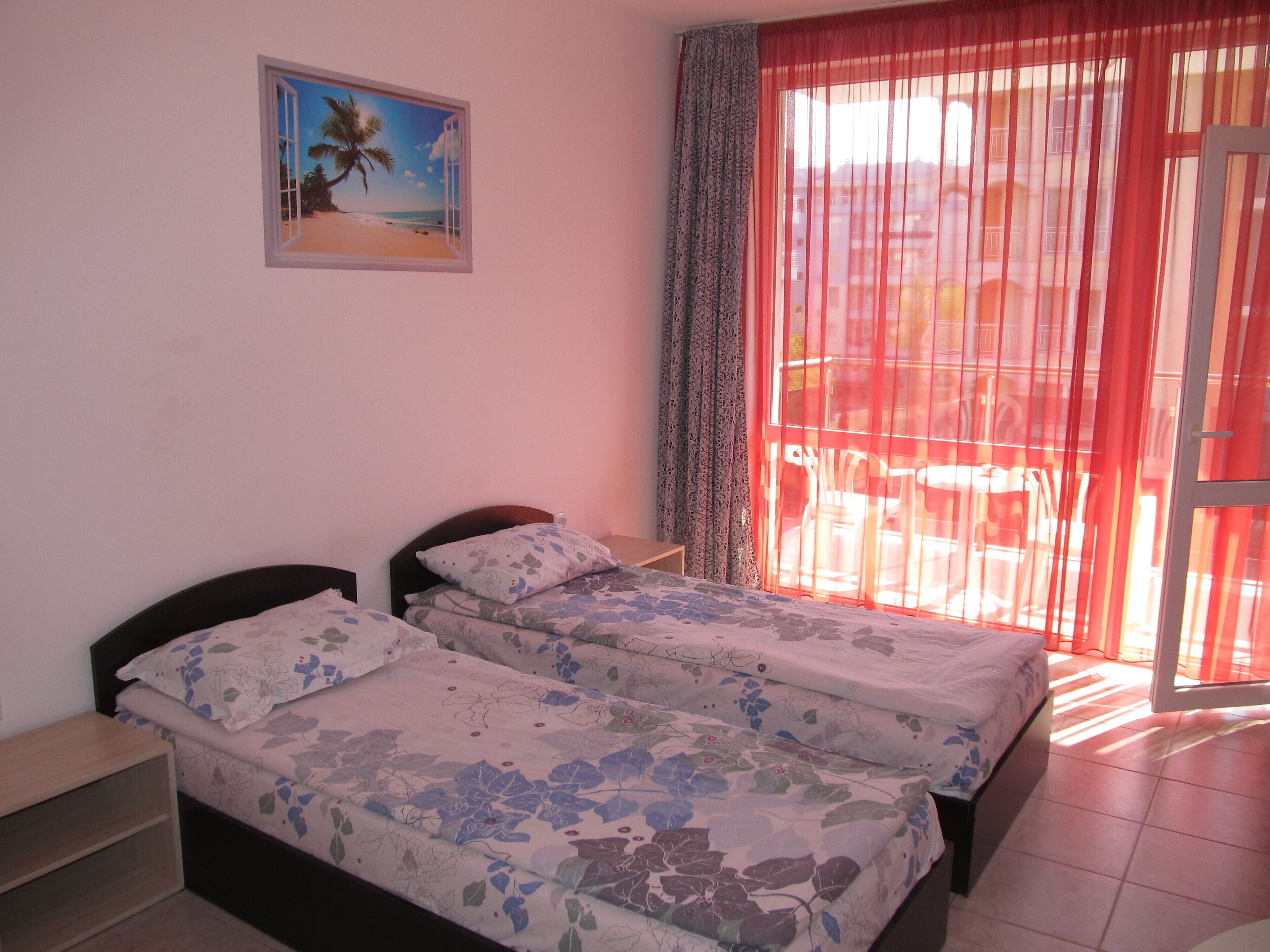 A bedroom with two beds, a window with a view of the outside, and a painting on the wall.