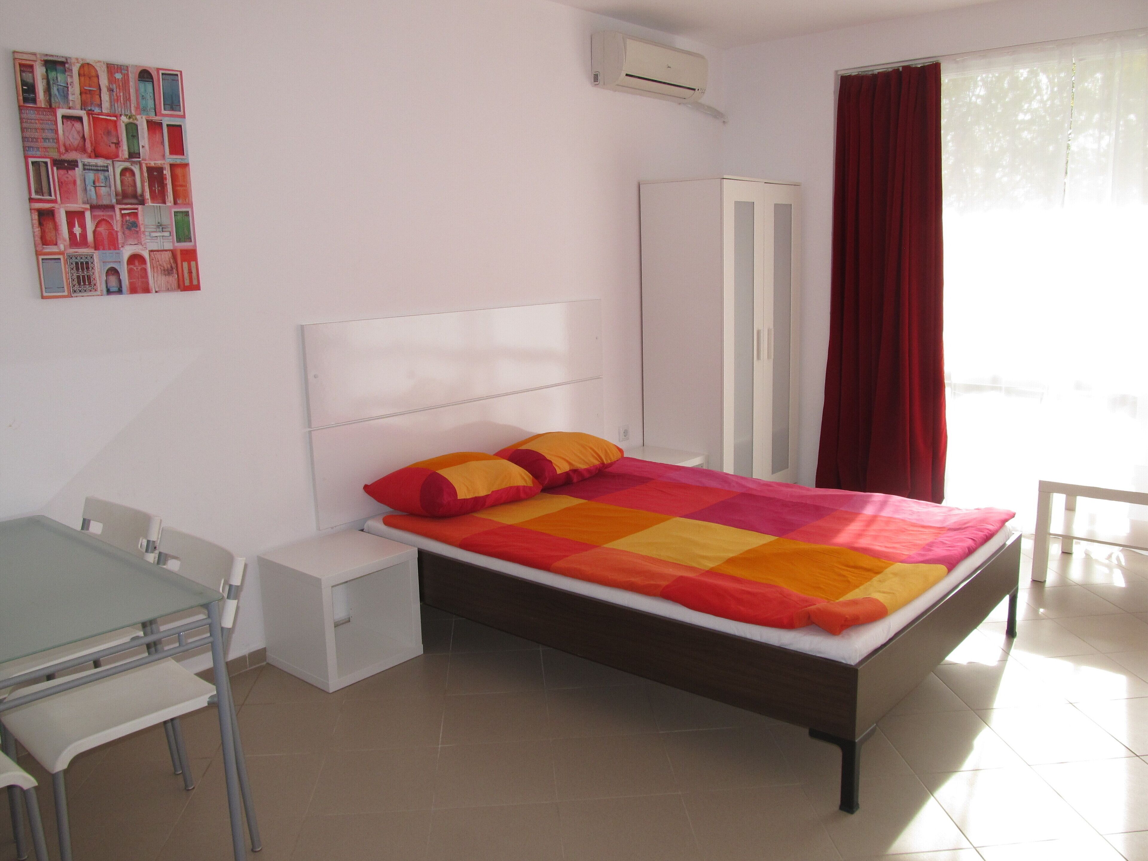 Un dormitorio con cama, escritorio, silla, armario y ventana con cortinas.