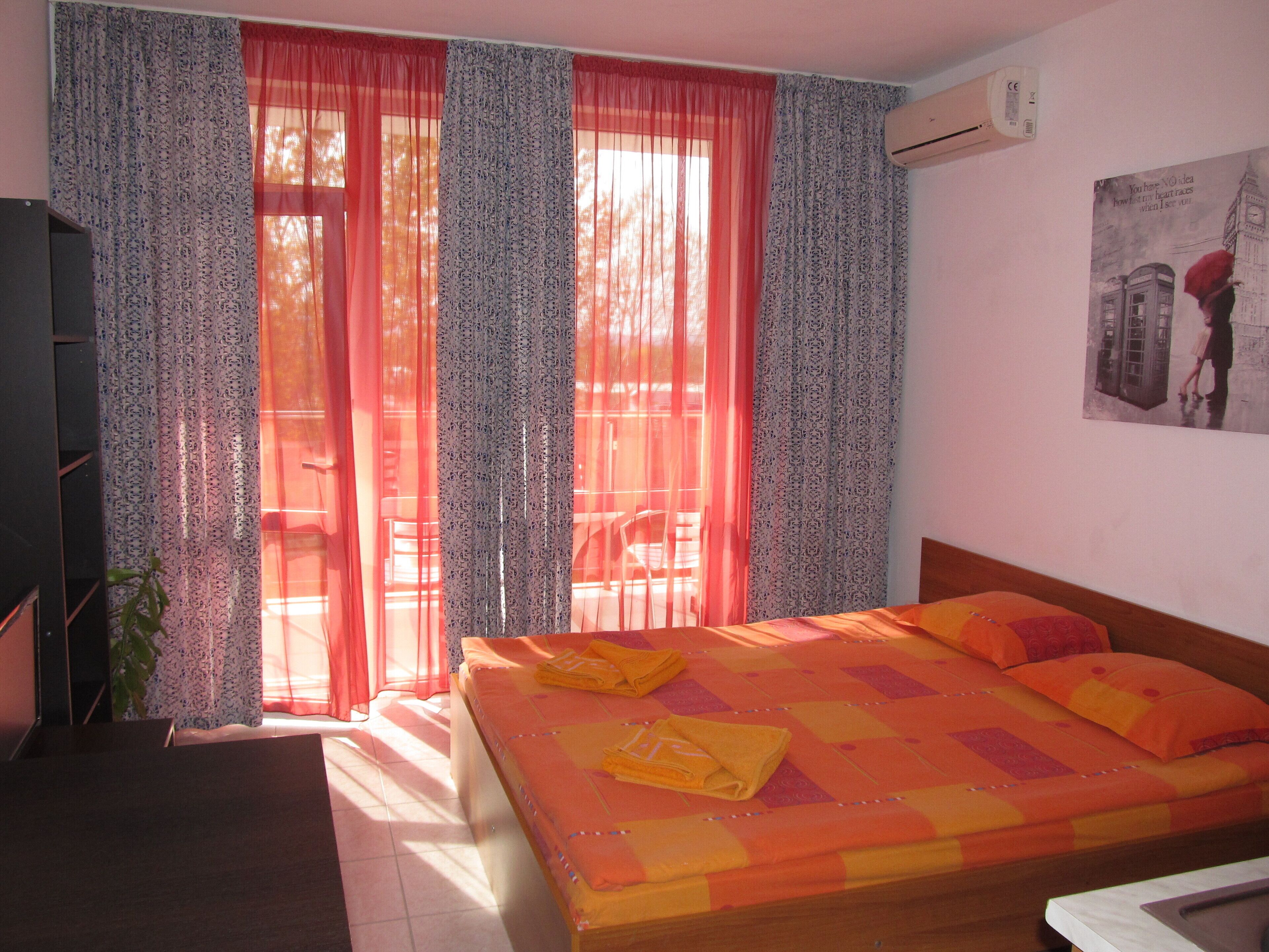 A bedroom with a bed, curtains, an air conditioner, and a poster on the wall.