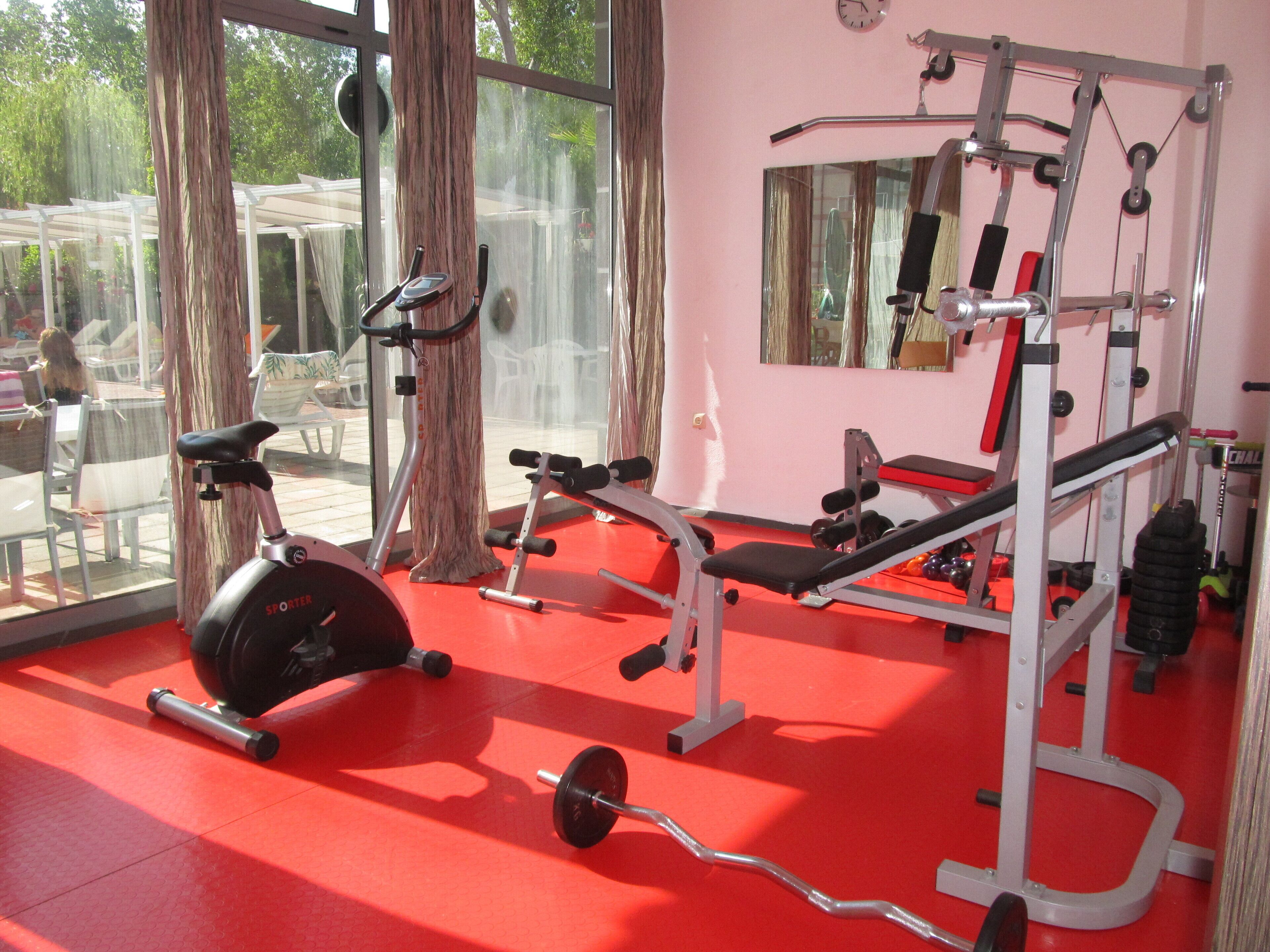 Een sportschool met trainingsapparatuur, grote ramen en een rode vloer.