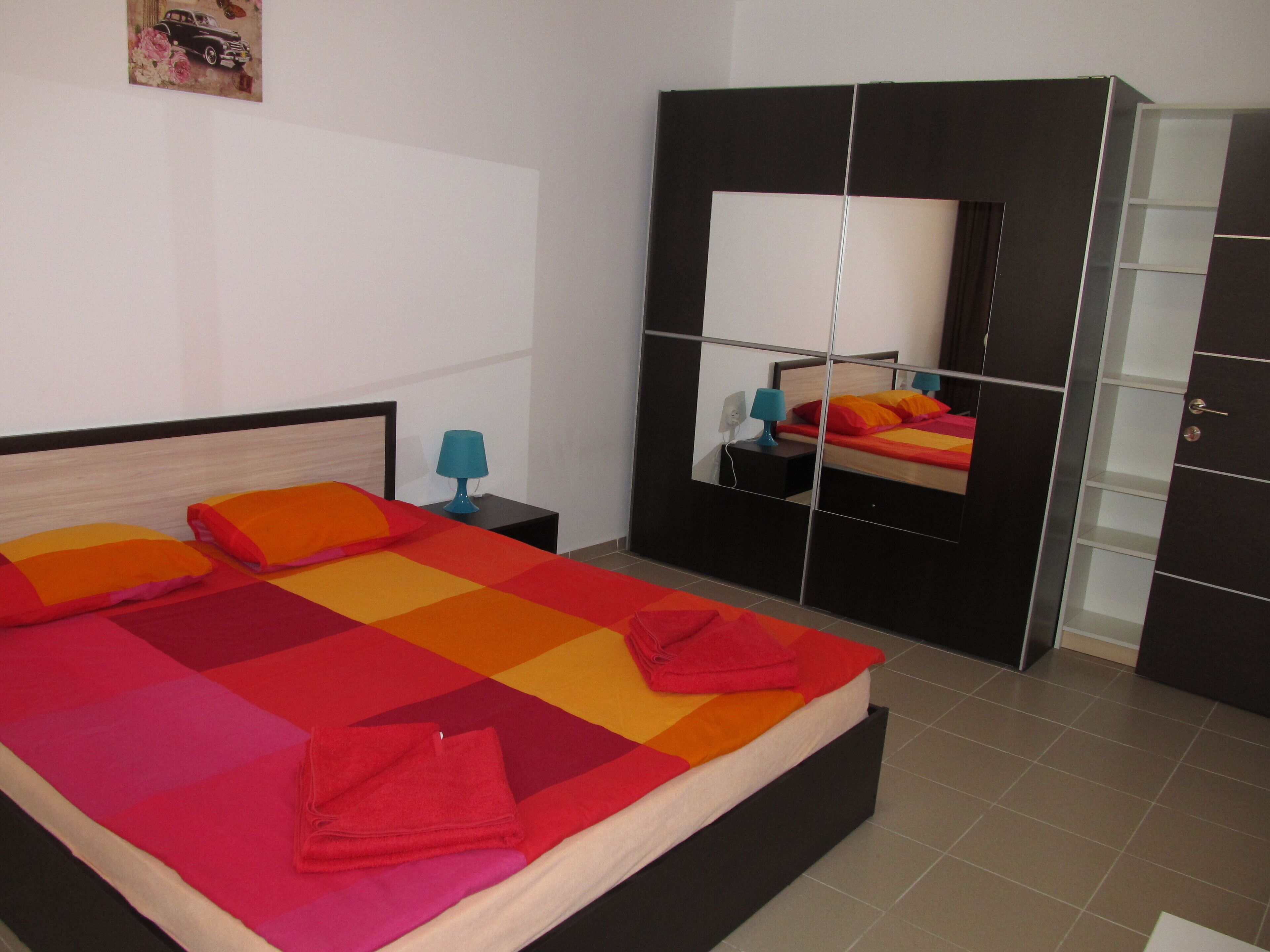 A neatly made bed with colorful bedding, a bedside table with a lamp, and a large wardrobe with mirrored doors.