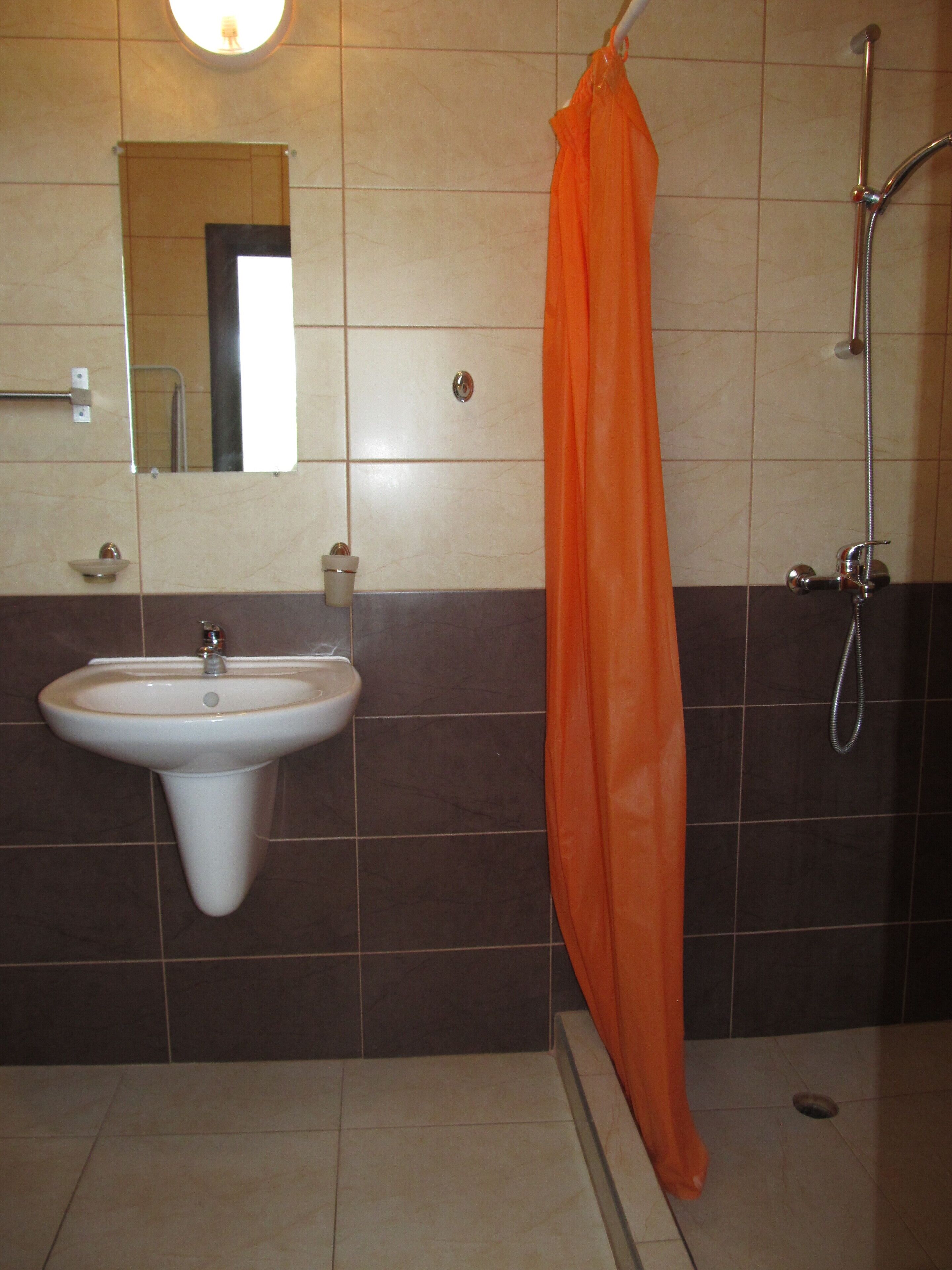 Une salle de bain avec un lavabo, un miroir, une douche et un rideau de douche orange.
