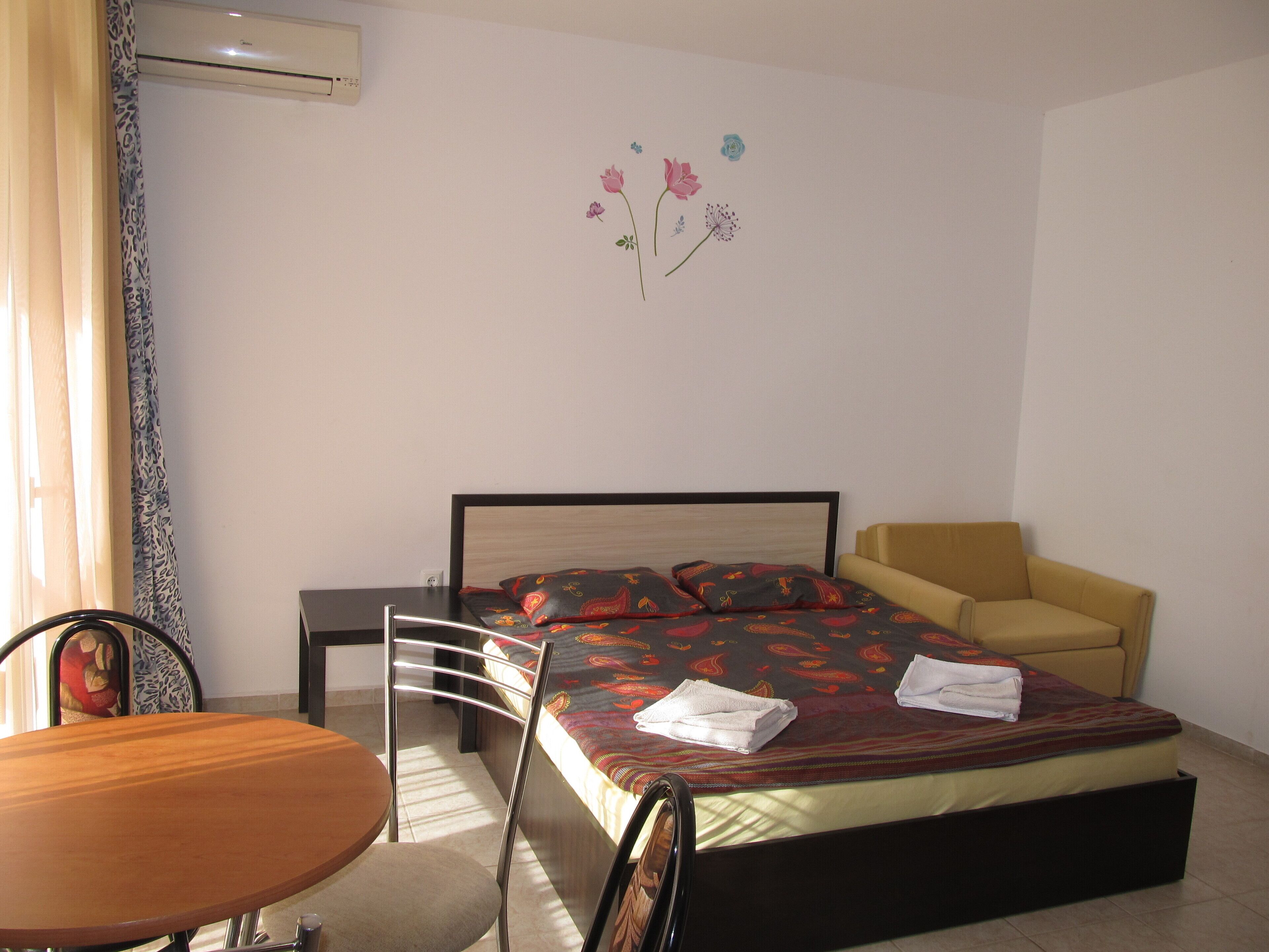 A bedroom with a bed, a chair, a table, and a wall decoration.