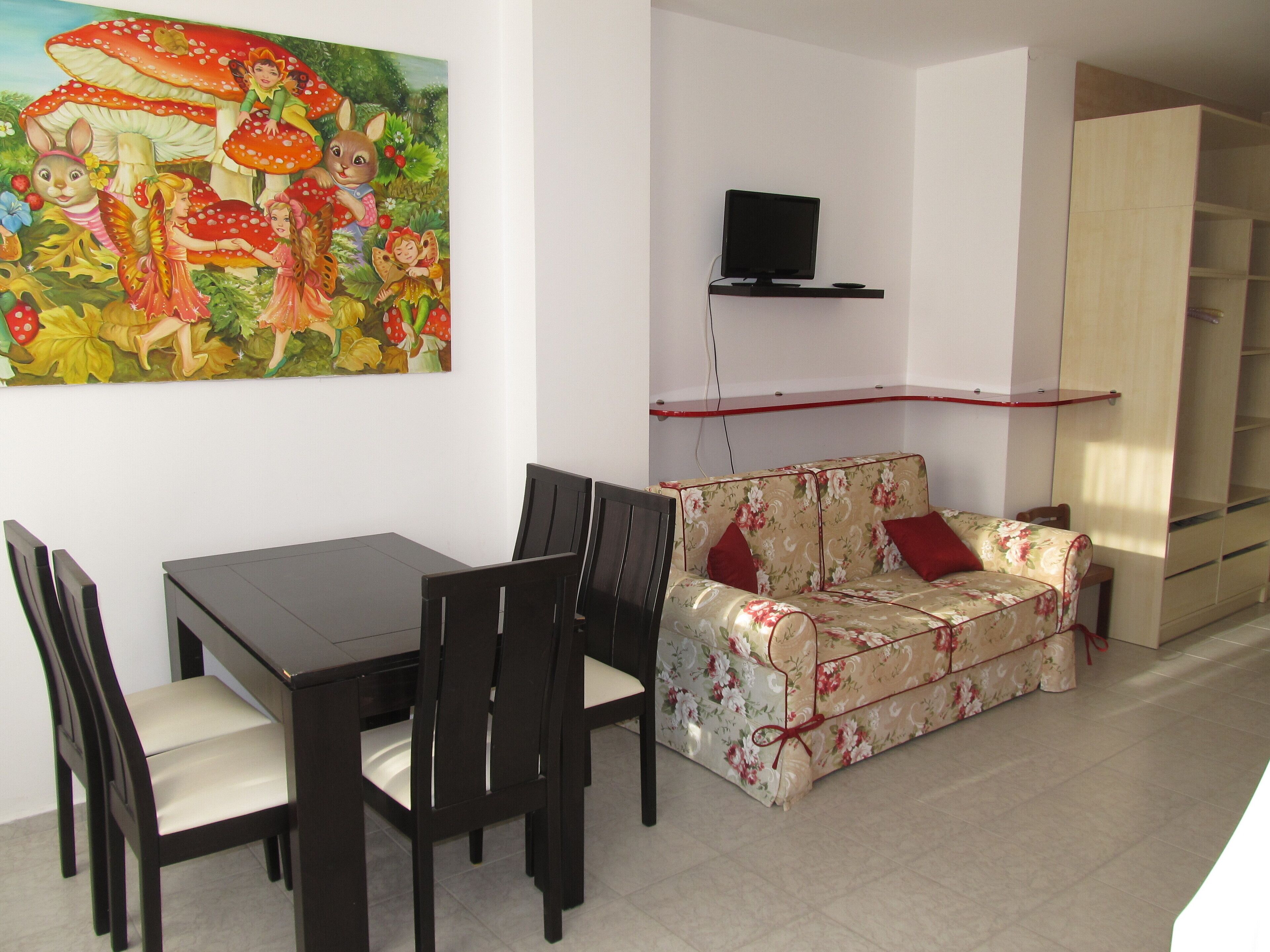 Un comedor con una mesa y sillas, un sofá floral, un televisor en un estante y un armario.