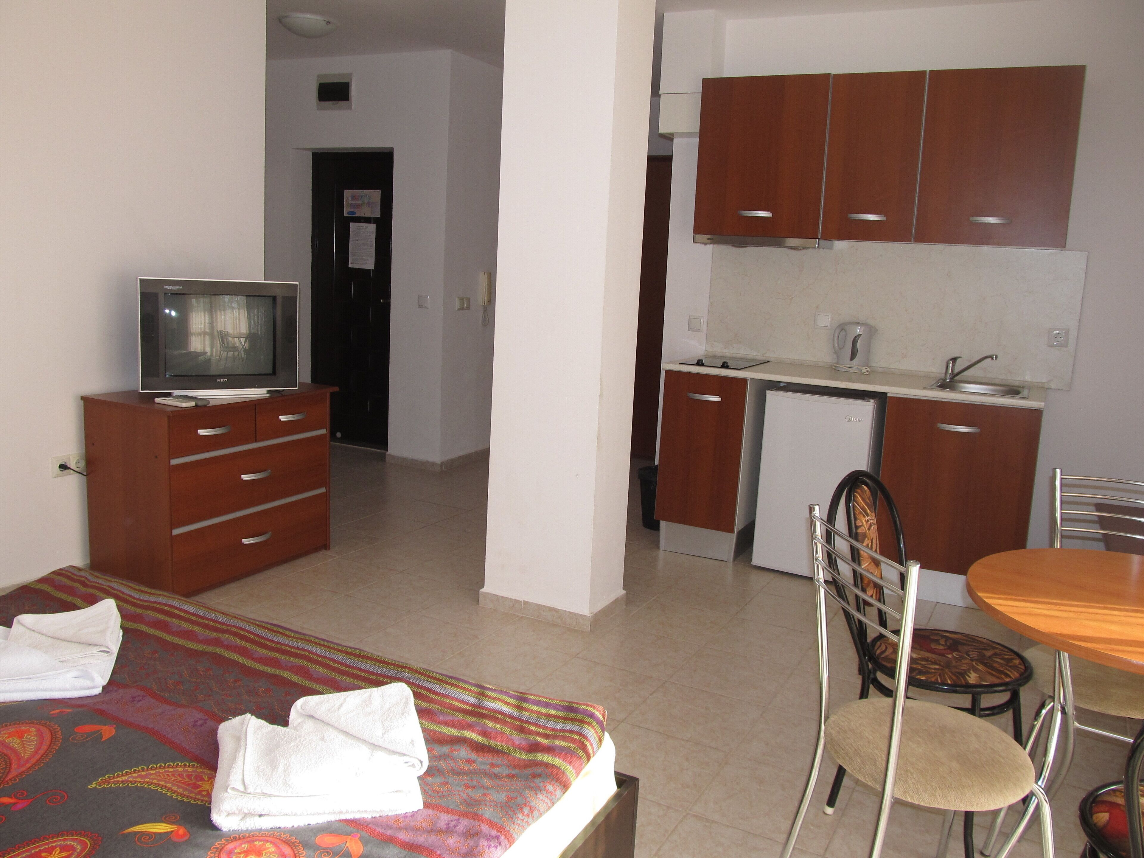 Ein Hotelzimmer mit Bett, Fernseher, einer kleinen Küchenzeile und einem Essbereich.