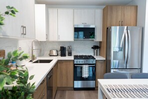 Une cuisine moderne avec des meubles blancs, un réfrigérateur en acier inoxydable, une cuisinière à gaz et un four à micro-ondes.