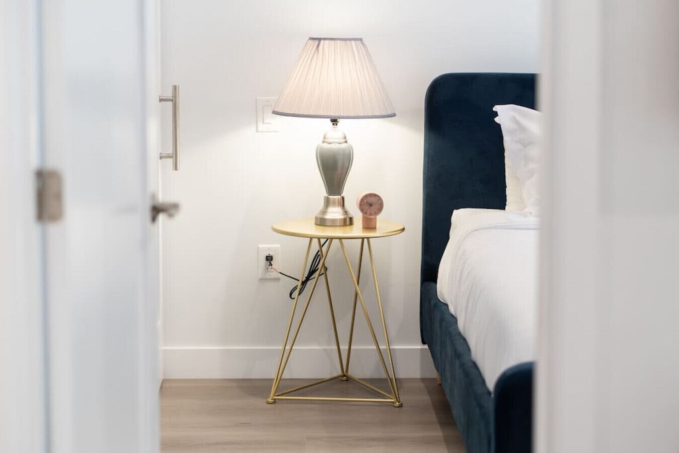 Una habitación de hotel con una cama, una mesita de noche con lámpara y un enchufe.