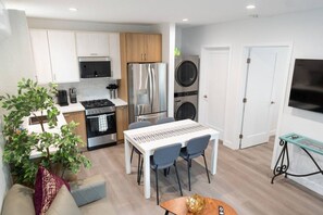 Une cuisine moderne équipée d’une cuisinière, d’un four, d’un four à micro-ondes et d’un réfrigérateur. On y trouve également un coin repas avec une table et des chaises. Une machine à laver est visible au fond.