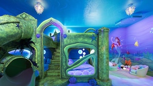Un espace de jeux sur le thème du monde sous-marin, avec un toboggan, une structure d’escalade et une décoration représentant une sirène.