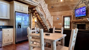 A rustic cabin interior with a wooden dining table, chairs, a refrigerator, a television, and a staircase. - Luxury Mountaintop Getaway with, Fire Pit, New Hot Tub, WiFi & Gorgeous Views! (Sevierville)