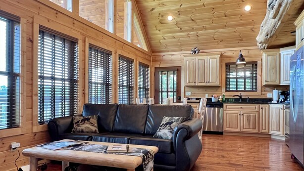 A spacious living area with a black leather sofa, wooden coffee table, and large windows with blinds. - Luxury Mountaintop Getaway with, Fire Pit, New Hot Tub, WiFi & Gorgeous Views! (Sevierville)