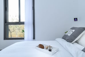 A neatly made bed with a tray of breakfast items, a pillow with 'BIG' text, and a window with a view of a building and bare trees.
