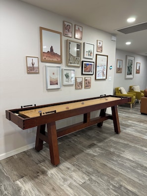 Een kamer met een tafelvoetbaltafel, een wand met ingelijste foto's en een gele fauteuil.