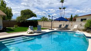 Ein Swimmingpool mit Liegestühlen und Sonnenschirmen, umgeben von einer angelegten Grünfläche und Palmen.