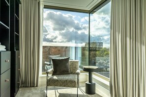 A modern room with a large window, a patterned armchair, a small round table, and a black cabinet.