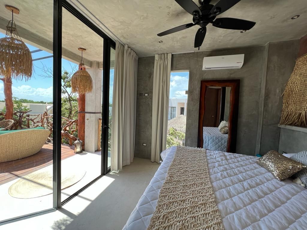 A bedroom with a bed, ceiling fan, and large windows.