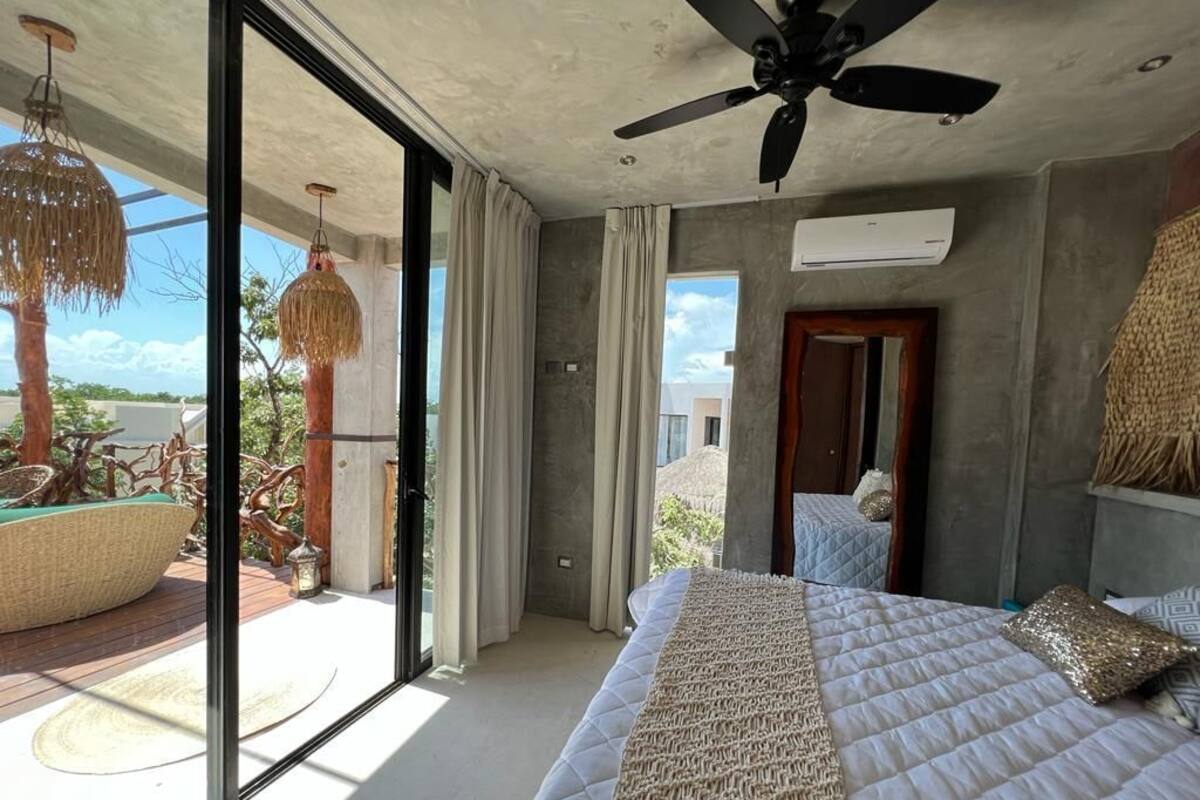 Un dormitorio con cama, ventilador de techo y ventanas amplias.