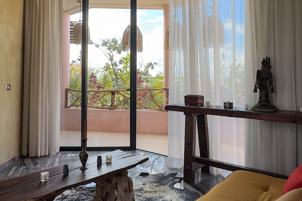 Habitación con ventilador de techo, un sofá, una mesa con adornos y vistas al exterior.