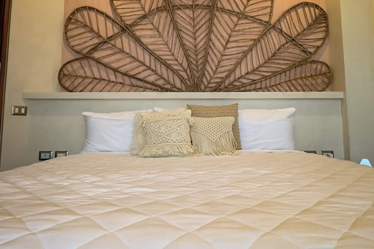 Una cama con edredón acolchado, decoración con diseño de hojas en la pared y un ventilador de techo.