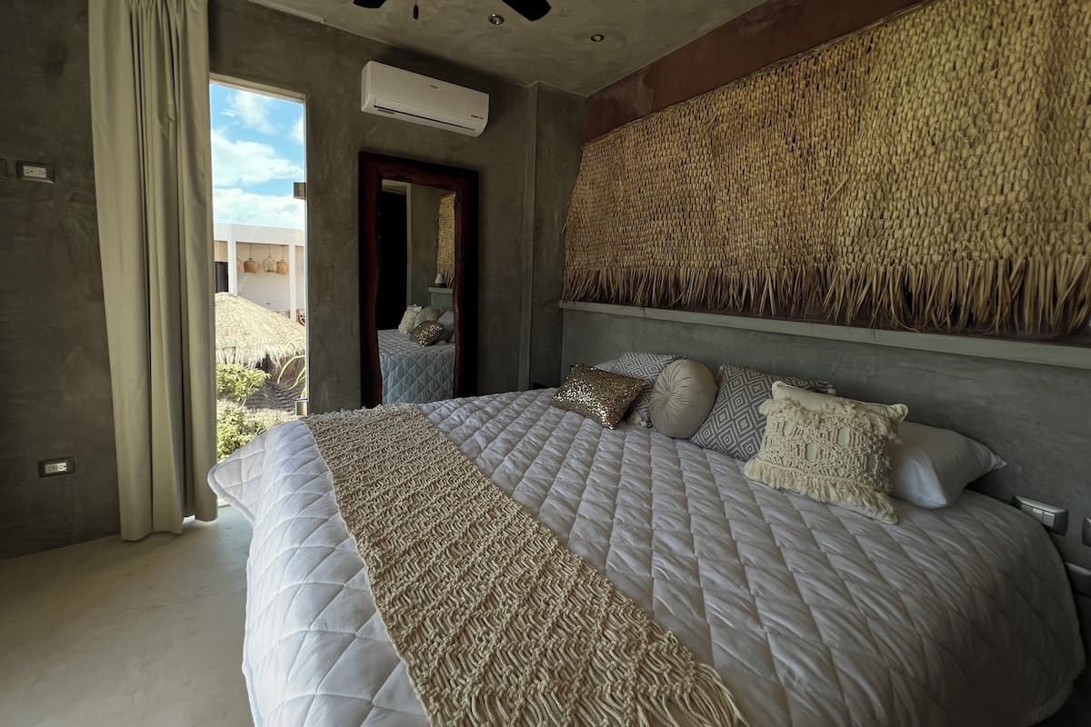 Un dormitorio con una cama grande, un ventilador de techo, un aire acondicionado y un tapiz de pared tejido.