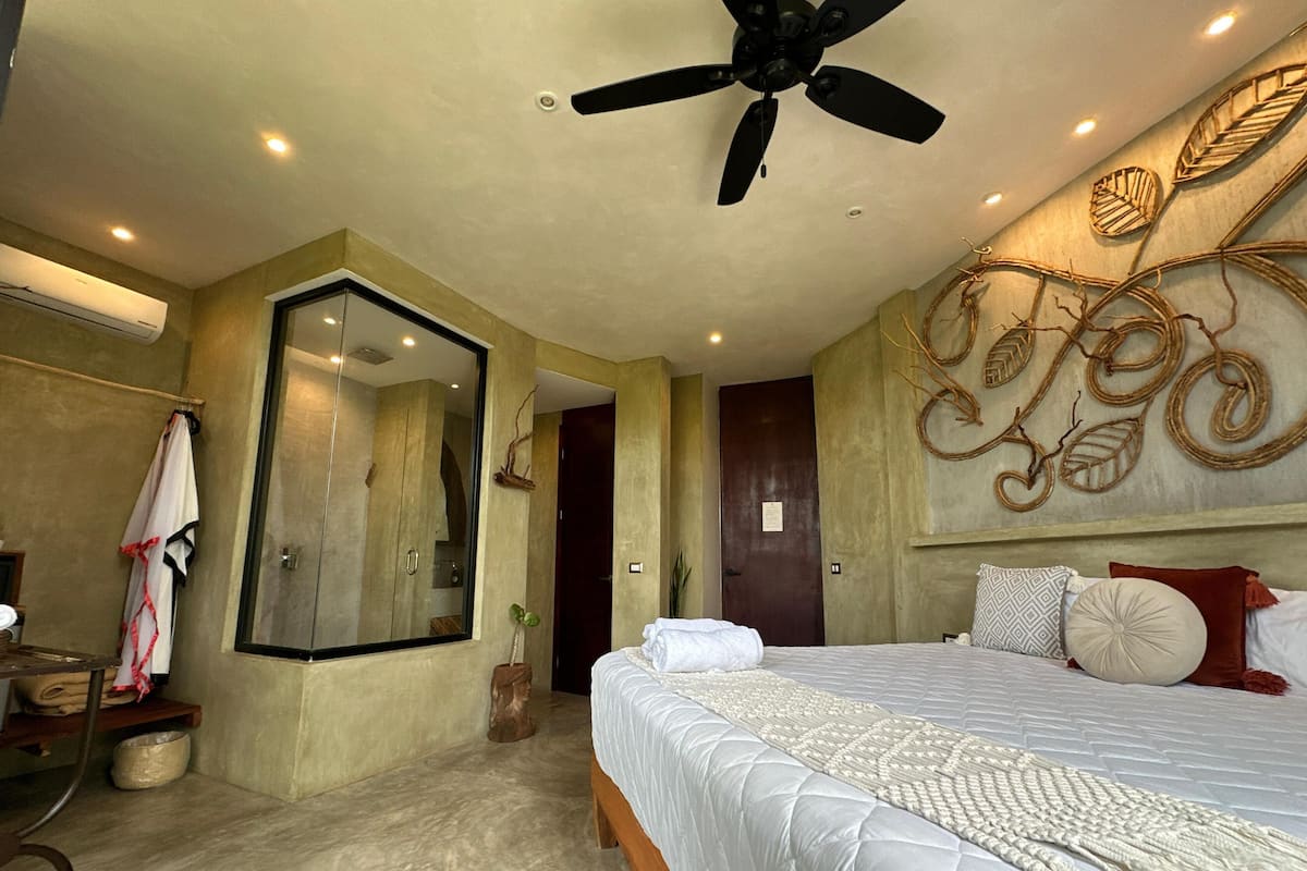 Un dormitorio con una cama grande, un ventilador de techo, un espejo y un diseño decorativo de hoja en la pared.