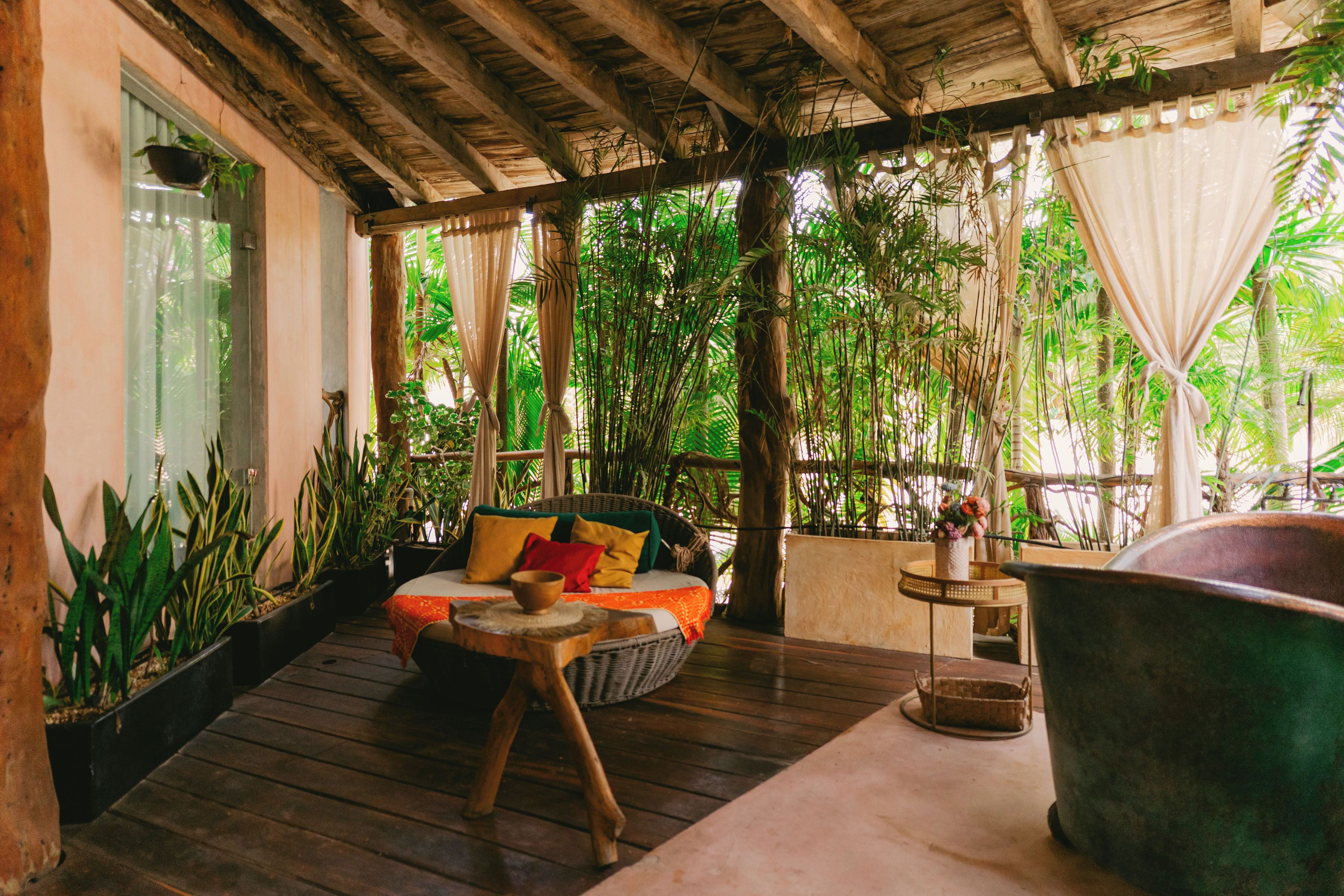 A wooden deck with a wicker sofa, a large metal basin, and lush tropical plants.
