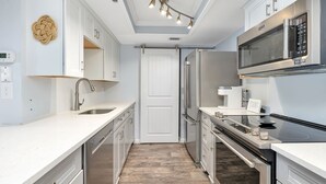 A modern kitchen with white cabinetry, stainless steel appliances, and a wooden floor. - St. Simons Beach Club, Oceanfront Pool, Fabulous Beach Access and More! (Saint Simons Island)