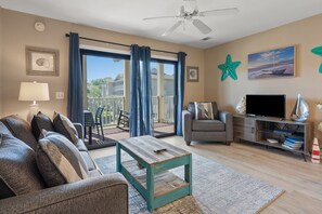Un salon comprenant un canapé, un fauteuil, une table basse, un meuble pour la télévision et un balcon avec vue.