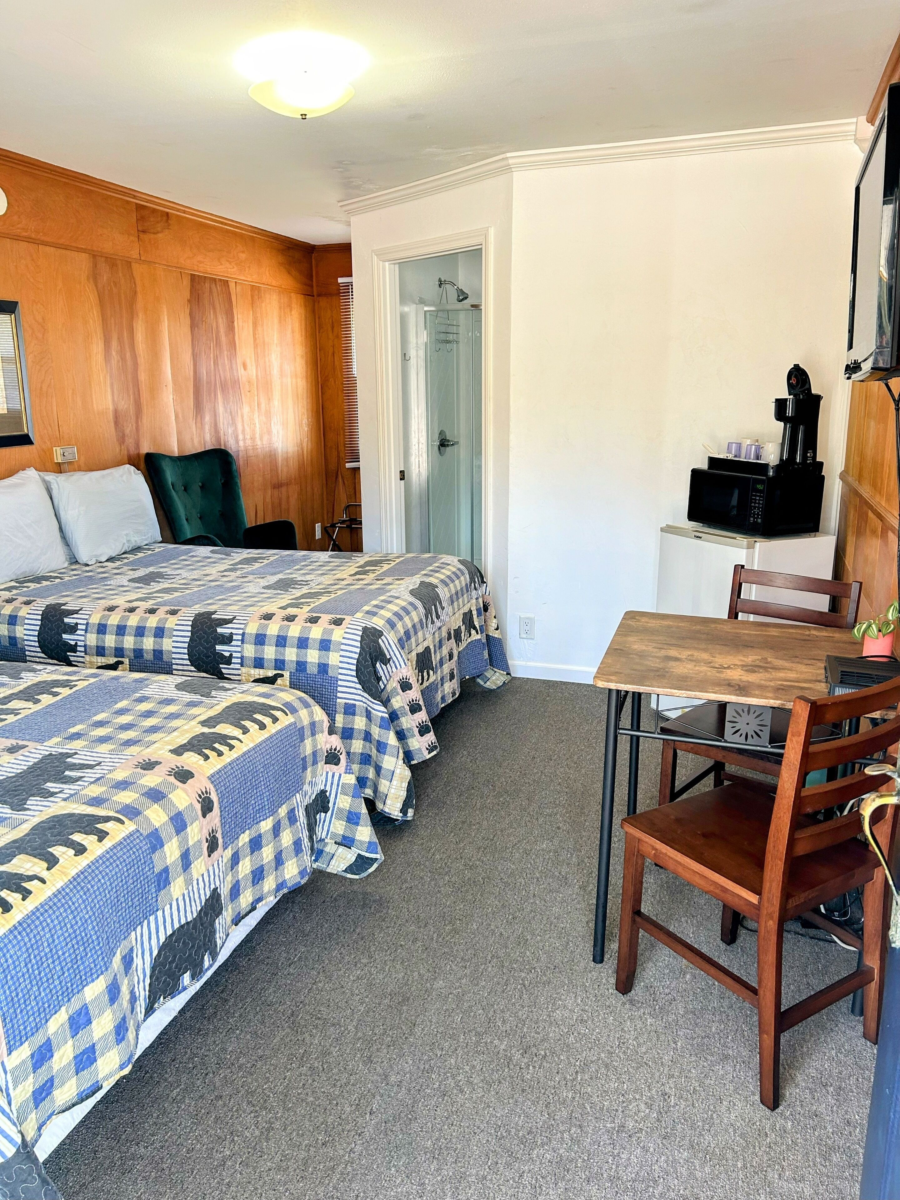 A hotel room with two beds, a wooden headboard, a small table with a microwave, and a chair.