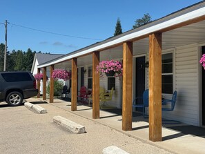 Une véranda couverte avec des piliers en bois, des sièges d’extérieur et des paniers de fleurs suspendus.