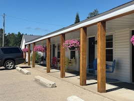 Un porche cubierto con columnas de madera, asientos exteriores y cestas de flores colgantes.