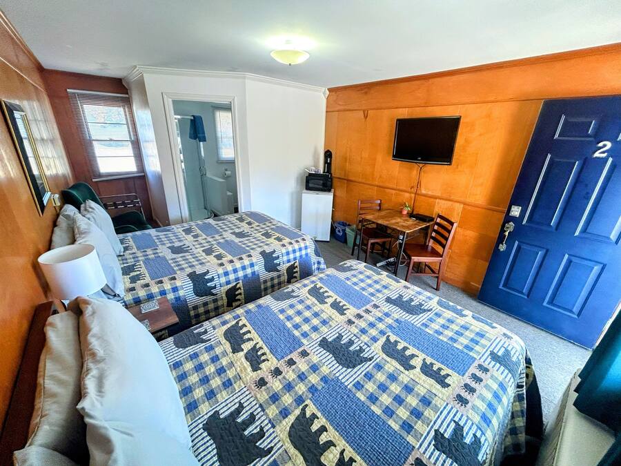 A hotel room with two beds, a small table, a chair, a TV, and a door with a number.