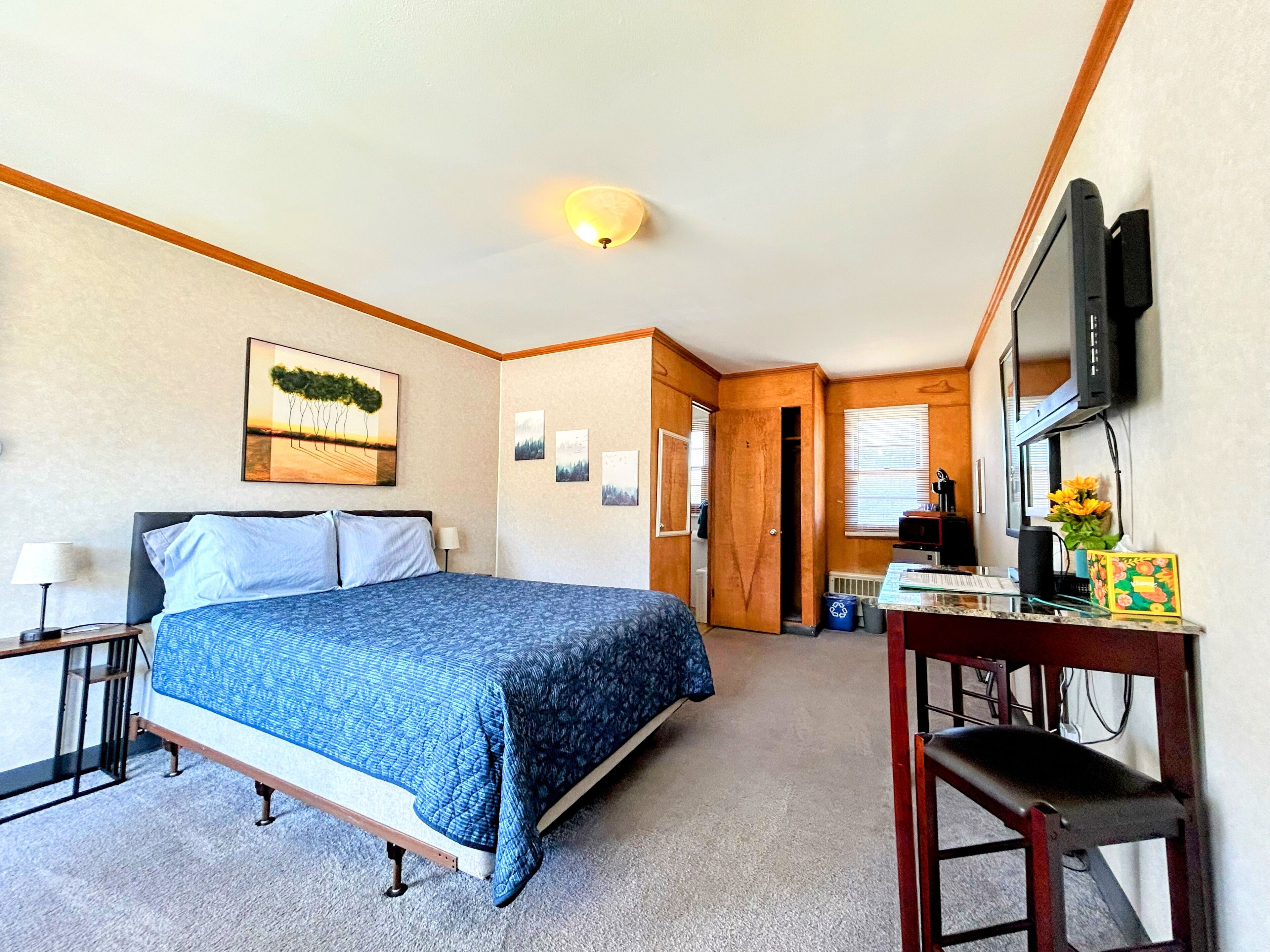 A bedroom with a bed, bedside tables, a desk with a chair, a television, and a door leading to another room.
