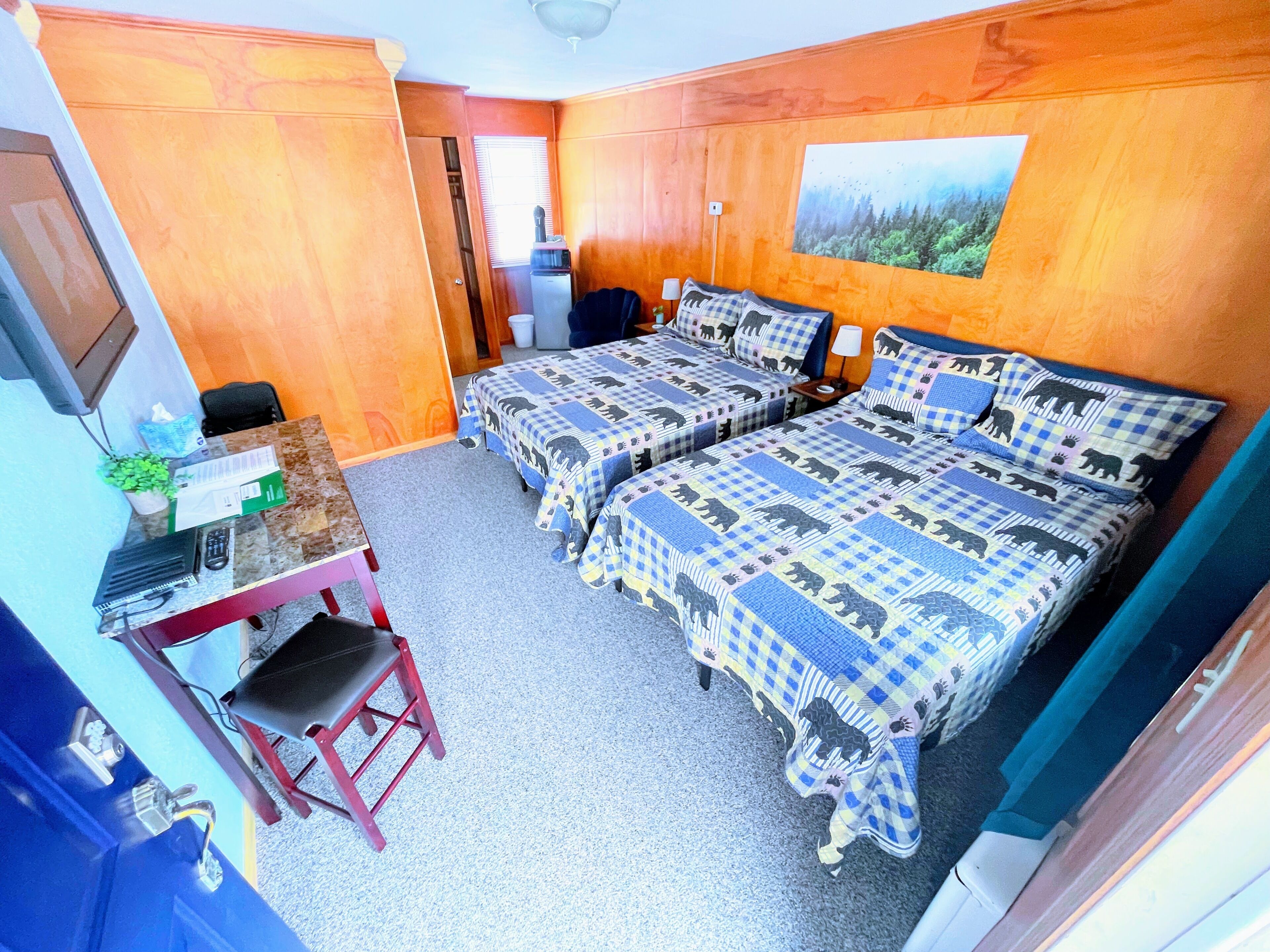 A room with two beds, a desk, a chair, a small table, and a painting on the wall.