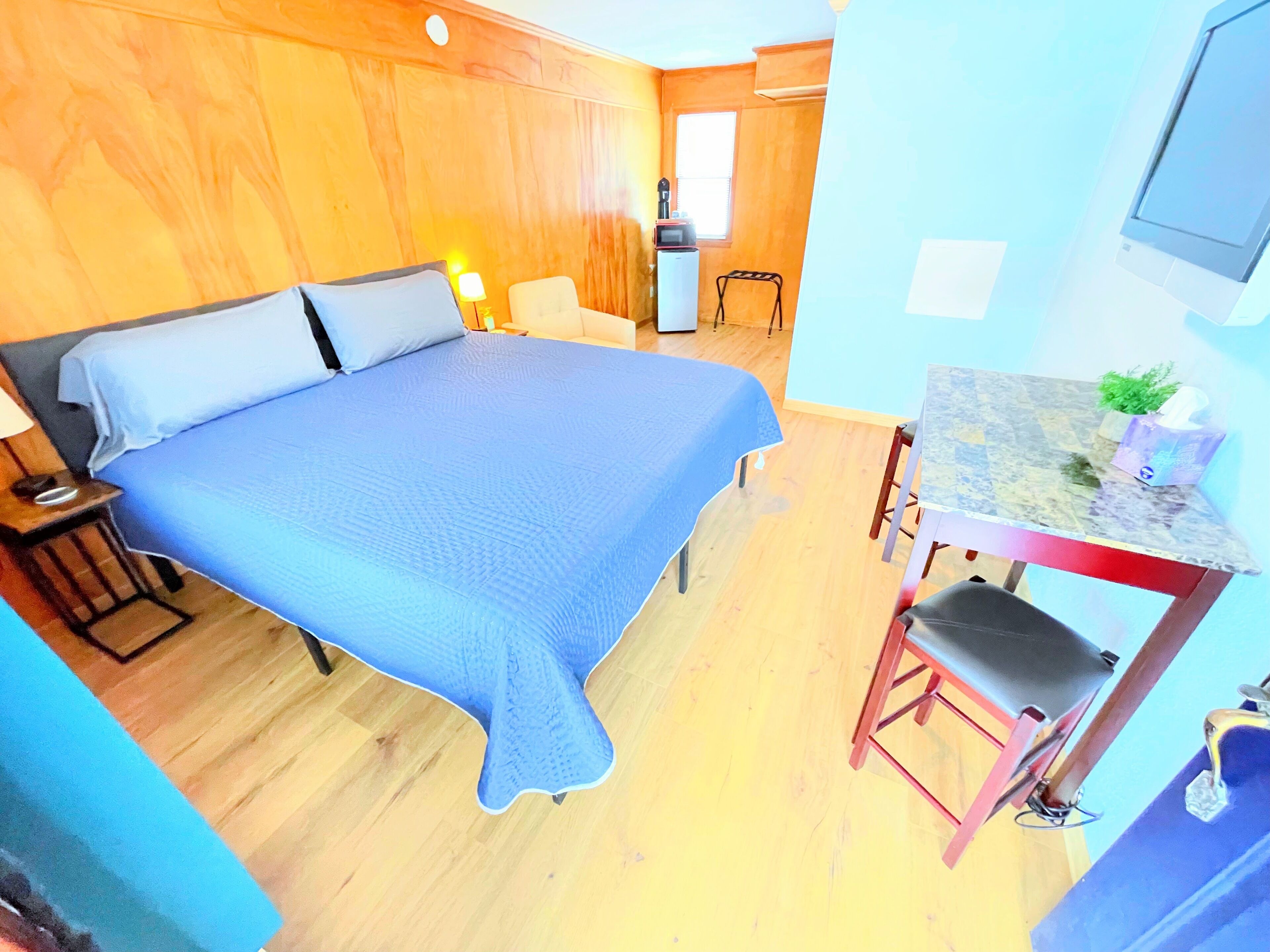 A room with a bed, a desk, and a chair. There is a window and a door in the background.