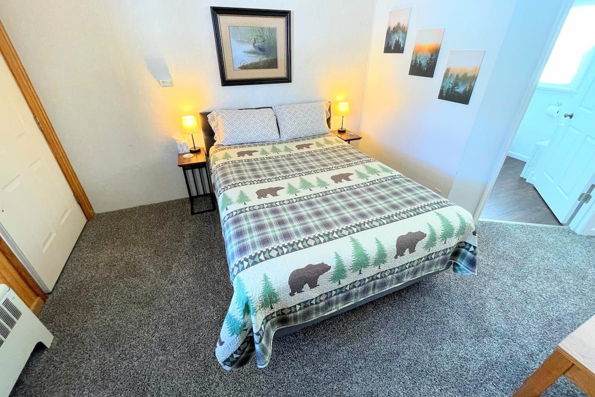 Un dormitorio con una cama, dos mesitas de noche con lámparas, un cuadro en la pared y una puerta.
